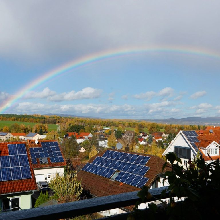 Haus verkaufen Adelsdorf: Wohngebiet mit Solardächern unter einem Regenbogen
